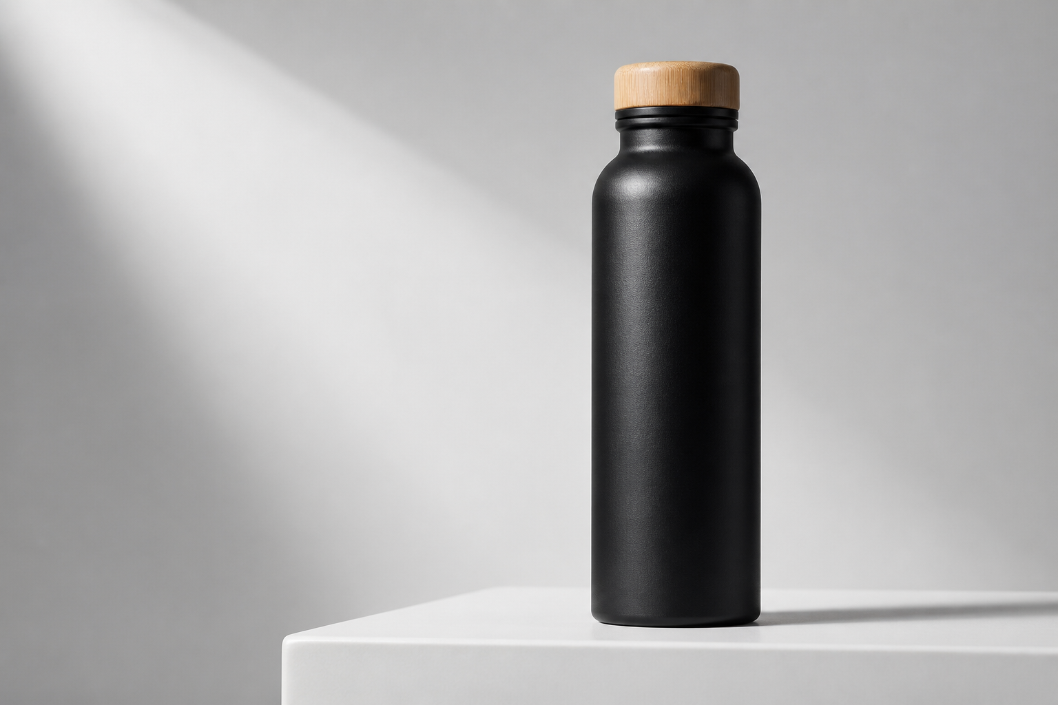 Matte black insulated bottle with bamboo cap photographed on a white acrylic pedestal