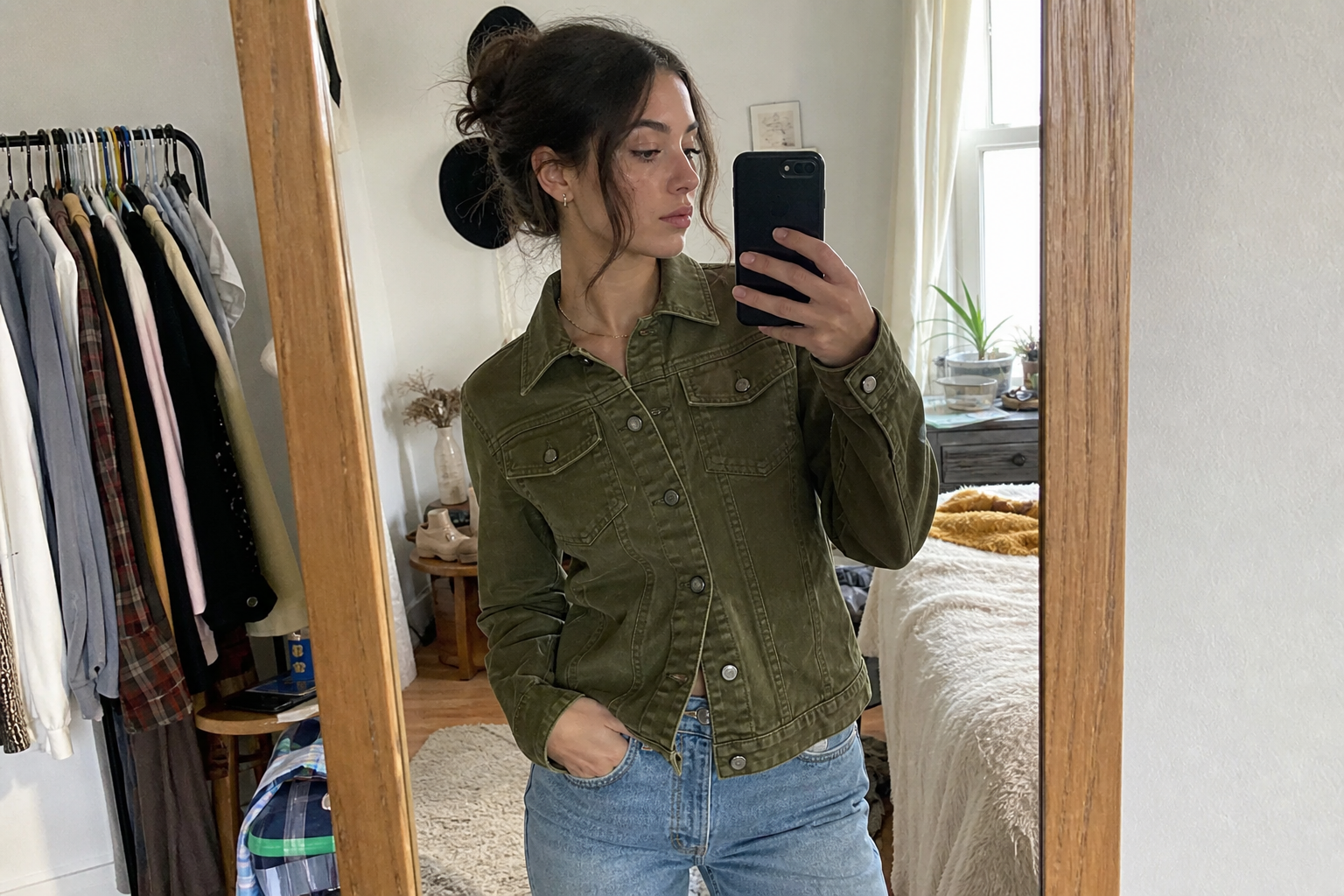 Casual mirror try-on photo of a woman wearing an olive denim jacket in a real bedroom